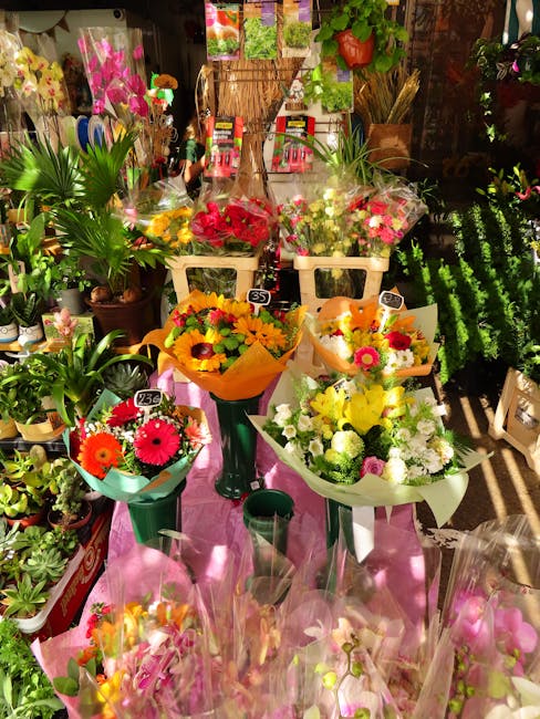 A display of vibrant floral arrangements from flowerdeliveryplumstead.co.uk, including bouquets of bright pink, yellow, orange, and white flowers wrapped in colorful paper and placed on tall green sta